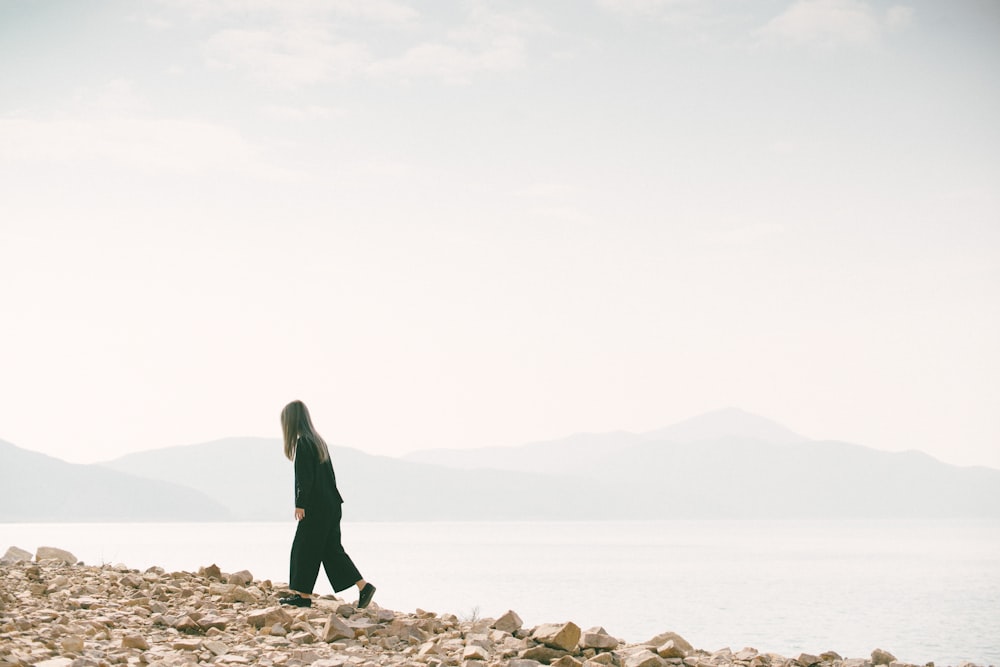 man walking on brown concrete rocks under gray sky