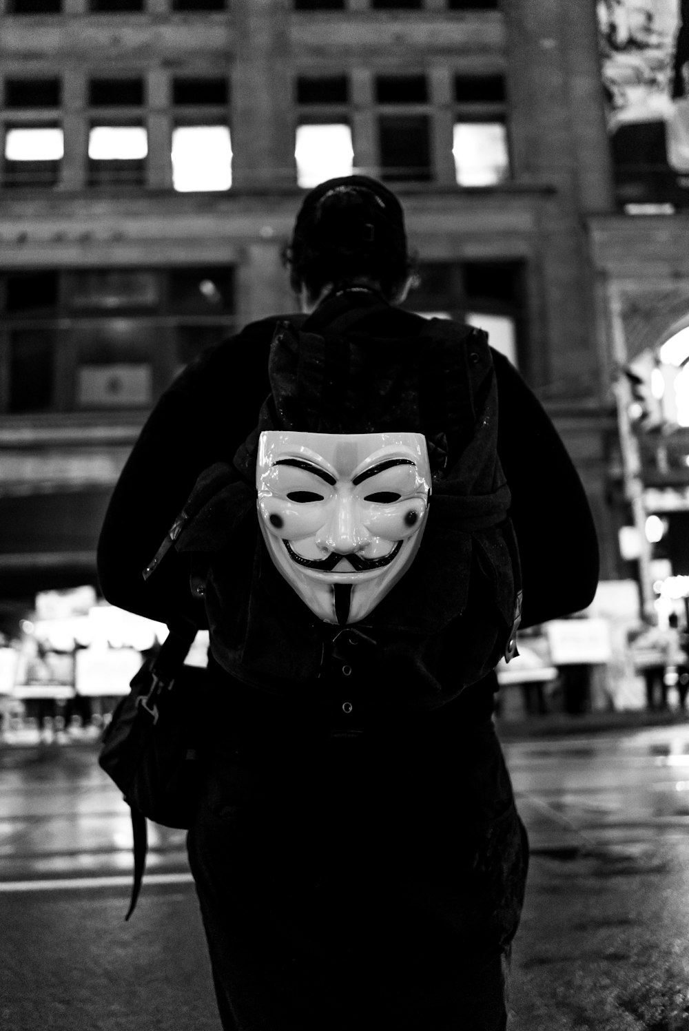 grayscale photography of person walking guy fawkes mask backpack