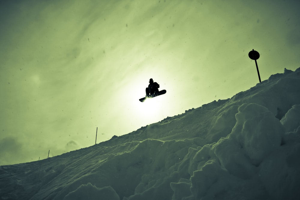 Silhouettenfotografie eines Mannes, der einen Snowboard-Stunt erstellt