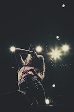 A singer performing passionately on stage with bright lights in the background.