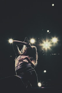 A person is fervently singing into a microphone on stage, with bright stage lights illuminating the background.