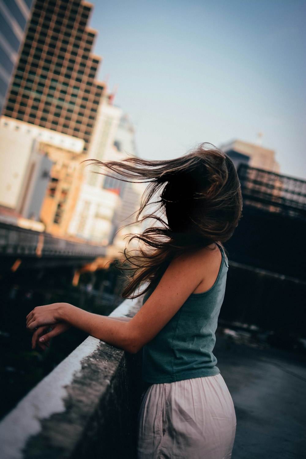 woman standing on black concrete pavement resting both arms of railing at daytime