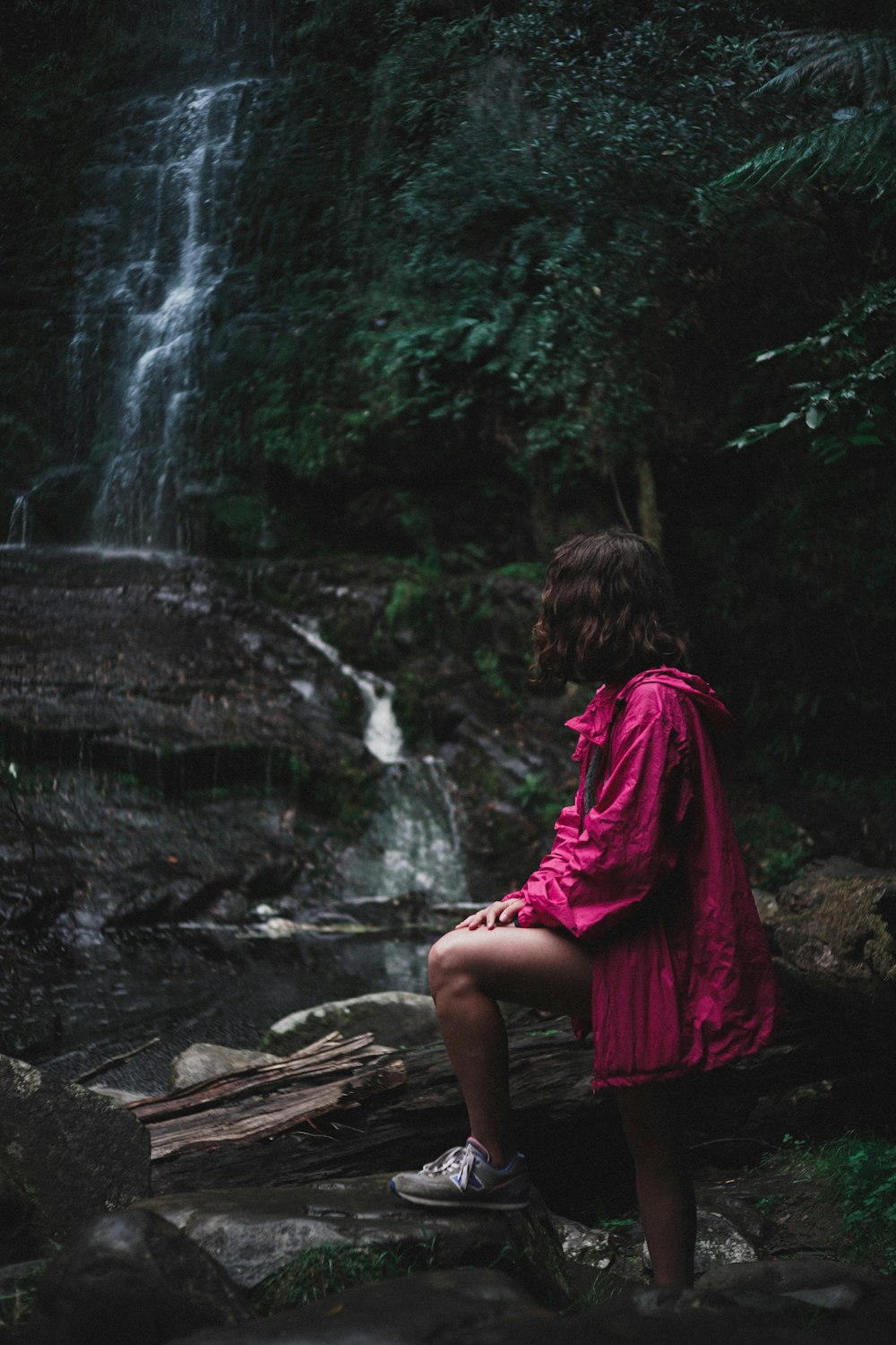 woman in purple jacket standing near waterfalls