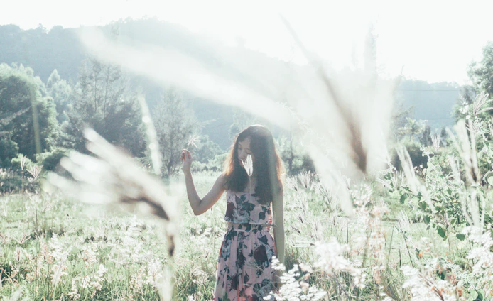 Sunlit serene meadow with models wearing light apricot pastel hippie-style clothing, evoking a Nordic-Greek inspired vibe.