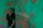 A person stands in front of a green background covered with orange graffiti-like patterns. The words 'MUSIC' are partially visible, adding an artistic and urban vibe to the scene.