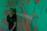 A person stands in front of a green background covered with orange graffiti-like patterns. The words 'MUSIC' are partially visible, adding an artistic and urban vibe to the scene.