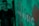 A blurred figure stands in front of a green background with a pattern and the word 'MUSIC' visible. The image has a pixelated digital display appearance.