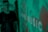 A blurred figure stands in front of a green background with a pattern and the word 'MUSIC' visible. The image has a pixelated digital display appearance.