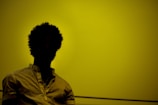 A silhouette of a person with curly hair against a yellow background, wearing a light-colored shirt.