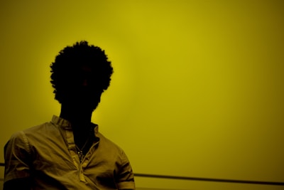 A silhouette of a person with curly hair against a yellow background, wearing a light-colored shirt.
