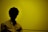 A silhouette of a person with curly hair against a yellow background, wearing a light-colored shirt.