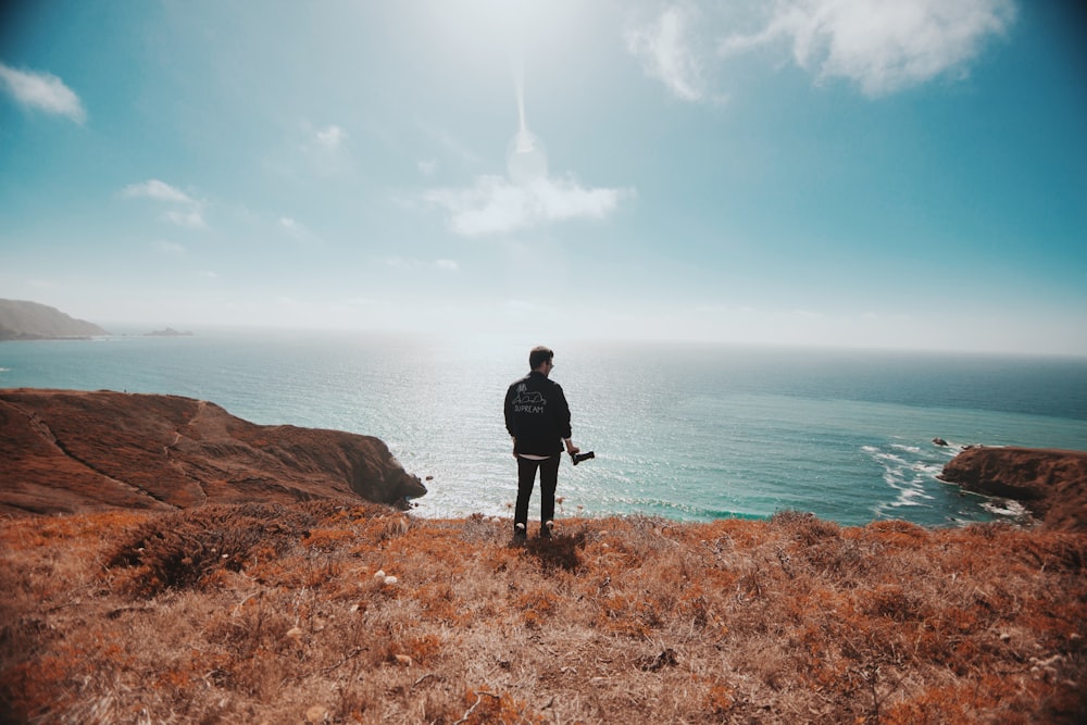 man in black jacket standing on brown grass