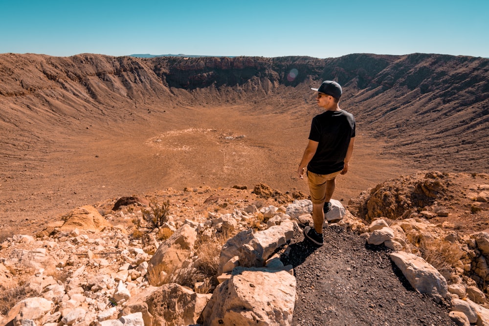 man wearing black shirt standing on rock formation during daytime