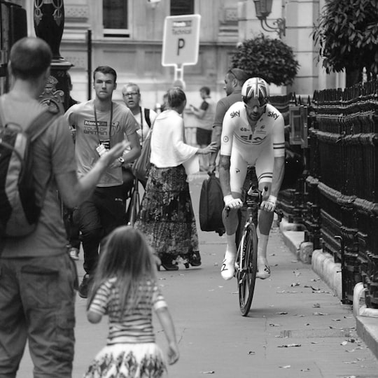 grayscale photo of man cycling beside group of people in Whitehall United Kingdom