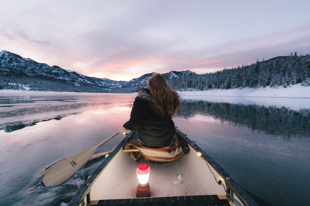 woman wearing black winter jacket sitting on boat paddling toward mountains