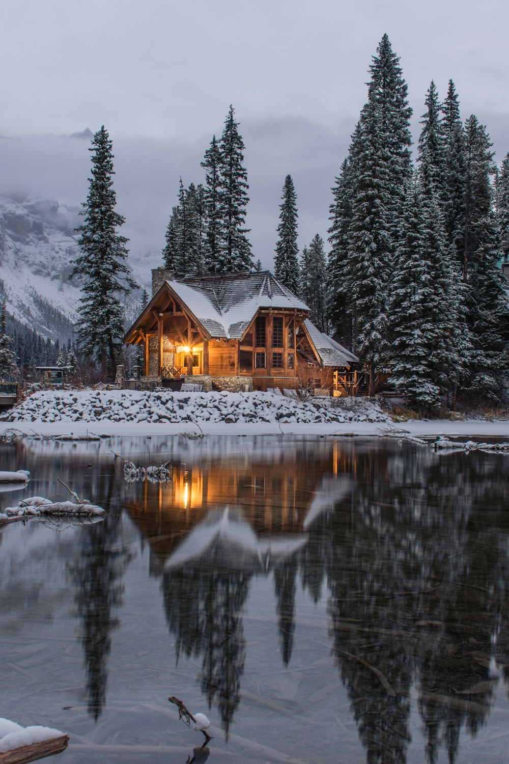 Casa de madeira perto de pinheiros e lagoa revestida com neve durante o dia