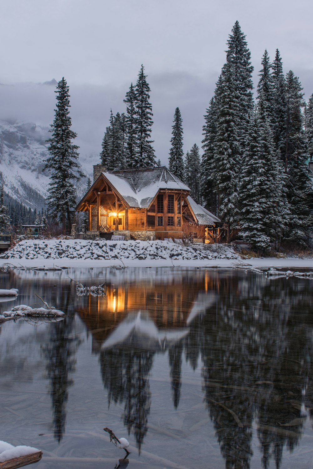 Holzhaus in der Nähe von Kiefern und Teich, der tagsüber mit Schnee bedeckt ist