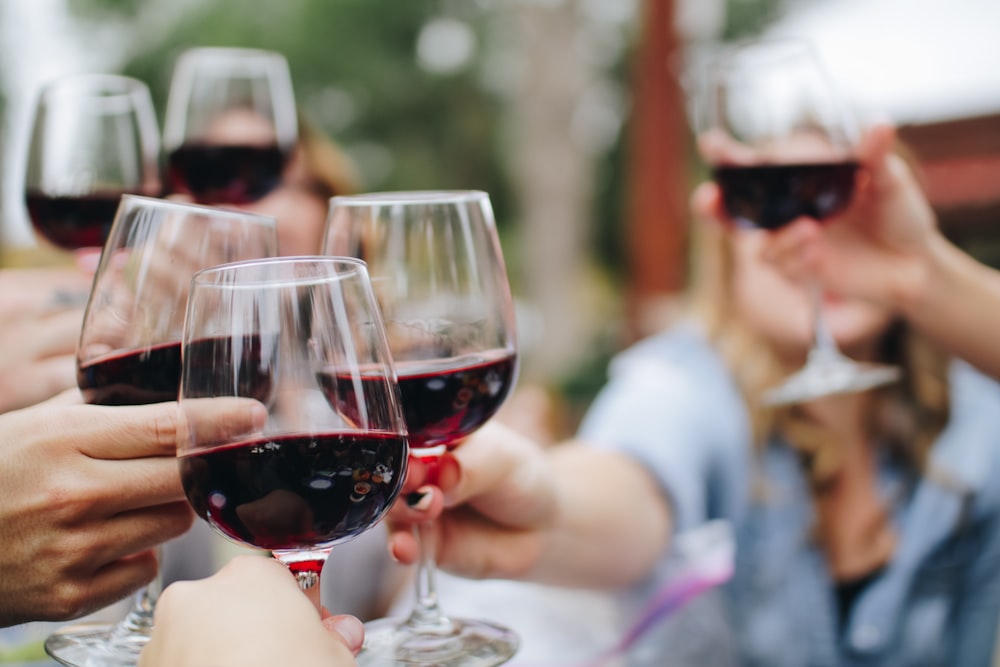 Young people celebrating together drinking red wine glasses on patio garden  at summer party. Diverse friends having fun cheering glasses during dinner  party. Friendship and celebration concept Stock Photo