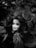 A doll's head with tangled hair is surrounded by foliage. The image is in black and white, creating a dramatic and eerie atmosphere. The hair appears disheveled, and the doll's expression is serene yet haunting due to the contrast with its surroundings.