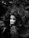 A doll's head with tangled hair is surrounded by foliage. The image is in black and white, creating a dramatic and eerie atmosphere. The hair appears disheveled, and the doll's expression is serene yet haunting due to the contrast with its surroundings.