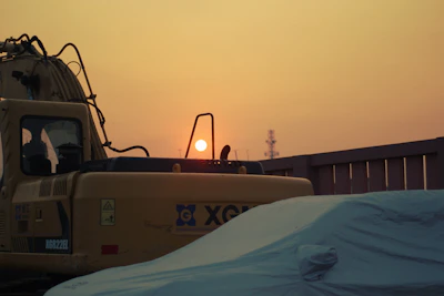 Heavy machinery compacting asphalt on a logistics park access road during sunset.