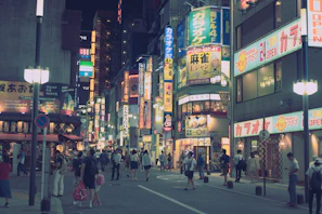 Bustling street scene in Osaka with neon signs and locals enjoying street food.