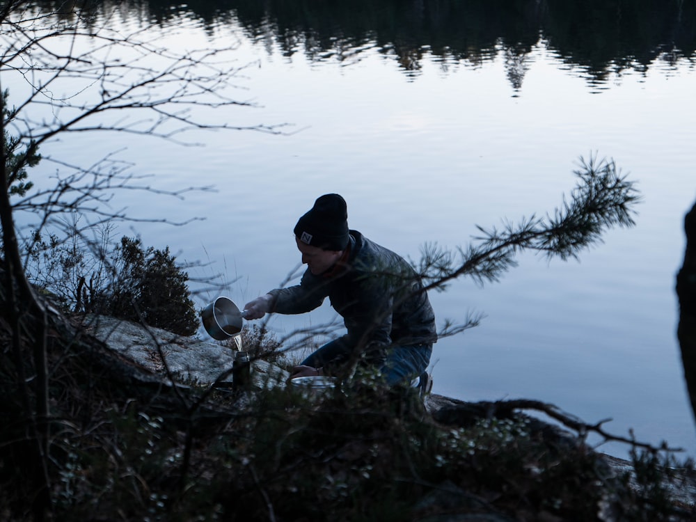 man pouring water from vacuum flask near lake during daytime