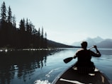 Kayaker paddling through calm waters reflecting towering pine trees in a serene lake.