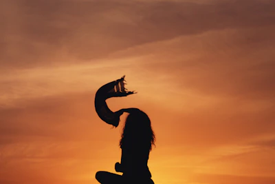 Sunset backdrop with a silhouette of a person wearing a flowy pastel scarf blowing in the breeze.