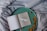 An open book with a simple, artistic illustration of a bird in the middle of one page, placed on a round, green tray. The text on the opposite page reads 'A little space to be creative'. Dried oak leaves are scattered on the tray, which rests on a softly wrinkled, grey fabric.