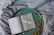 An open book with a simple, artistic illustration of a bird in the middle of one page, placed on a round, green tray. The text on the opposite page reads 'A little space to be creative'. Dried oak leaves are scattered on the tray, which rests on a softly wrinkled, grey fabric.