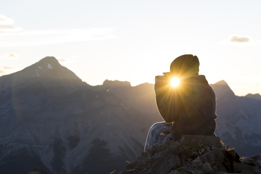 silhouette photography of person seating on rock in front of mountains