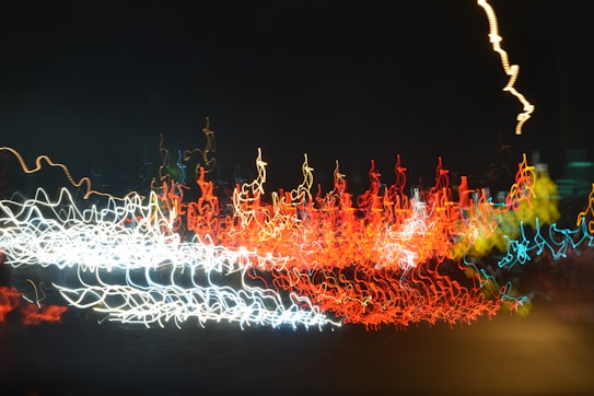 A long exposure photograph capturing vibrant light trails against a dark background. The image is composed of intersecting lines and squiggles of red, white, yellow, and blue lights, creating an abstract motion effect.