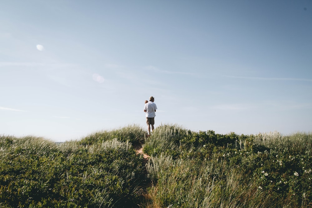 man carrying toddler standing on green field hill