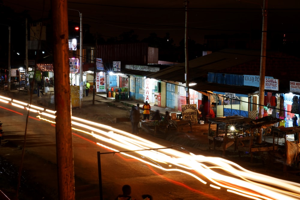 time lapse photography of race car lights on road beside stores