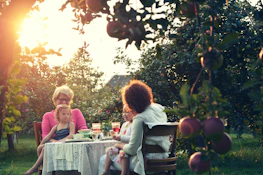 A multi-generational family gathered around a garden table, sharing stories and tasting honey.