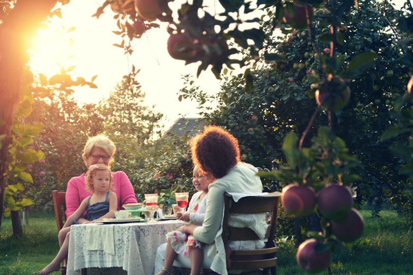 two women and holding two children while sitting outside house in the garden orchard