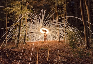 A woman playing a shamanic drum surrounded by forest and firelight.