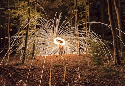 A woman playing a shamanic drum surrounded by forest and firelight.