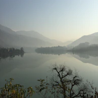 A serene landscape of misty mountains reflected in a still lake at dawn.