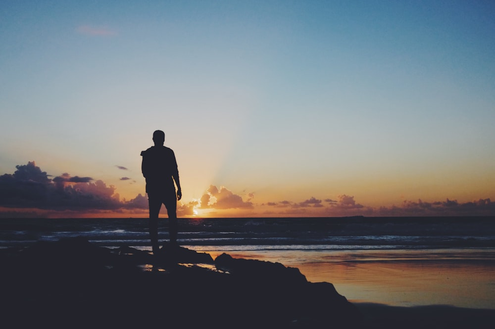 silhouette of man standing near shoreline