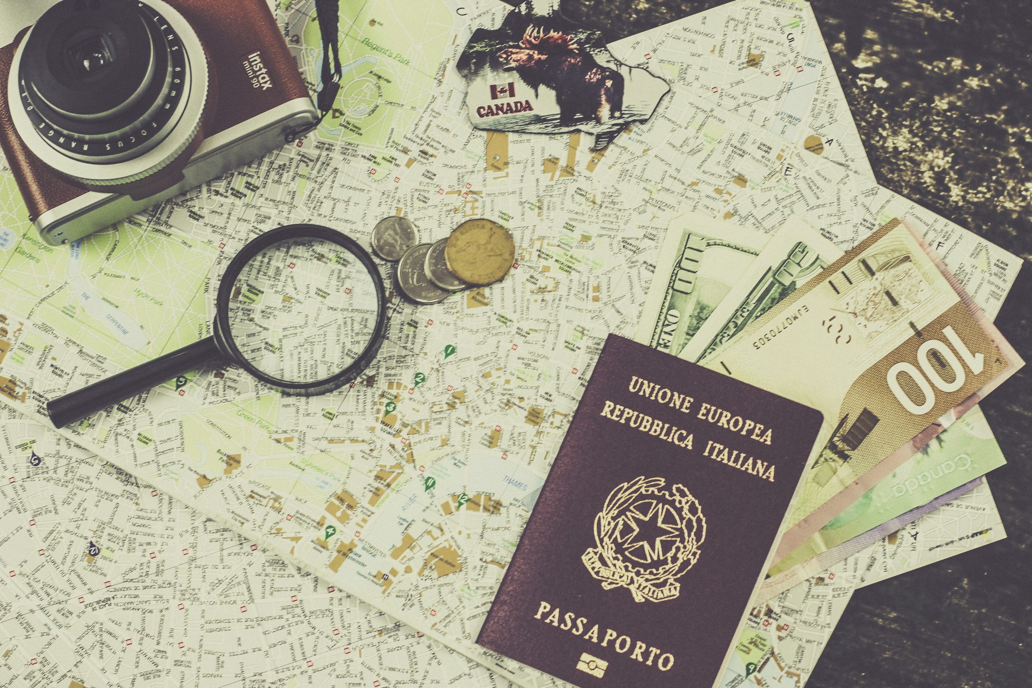 Passaporto italiano e macchinetta fotografica sopra delle mappe e banconote
