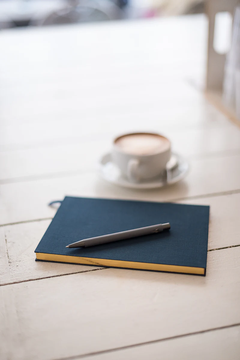 A person drafting notes at a desk beside a laptop and coffee