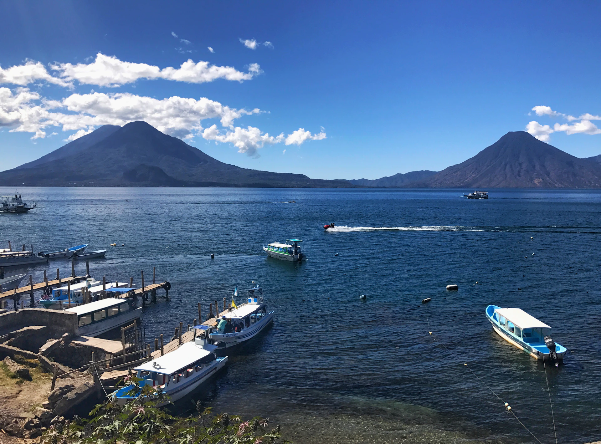 An engaging image of a group enjoying a scenic boat ride on a serene Guatemalan lake, framed by volcanoes under a clear blue sky.