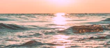 Sunset over calm ocean waters with gentle waves reflecting warm colors.