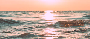 Sunset over calm ocean waters with gentle waves reflecting warm colors.