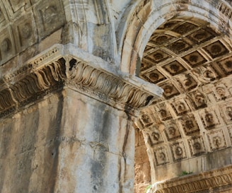 Detailed architectural elements of a historic stone structure featuring ornate carvings and intricate designs. The stonework includes decorative patterns on the arches and pillars, showcasing the craftsmanship of classical architecture.