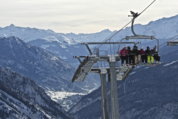 A chairlift carrying skiers above a snowy valley with rocky peaks beyond