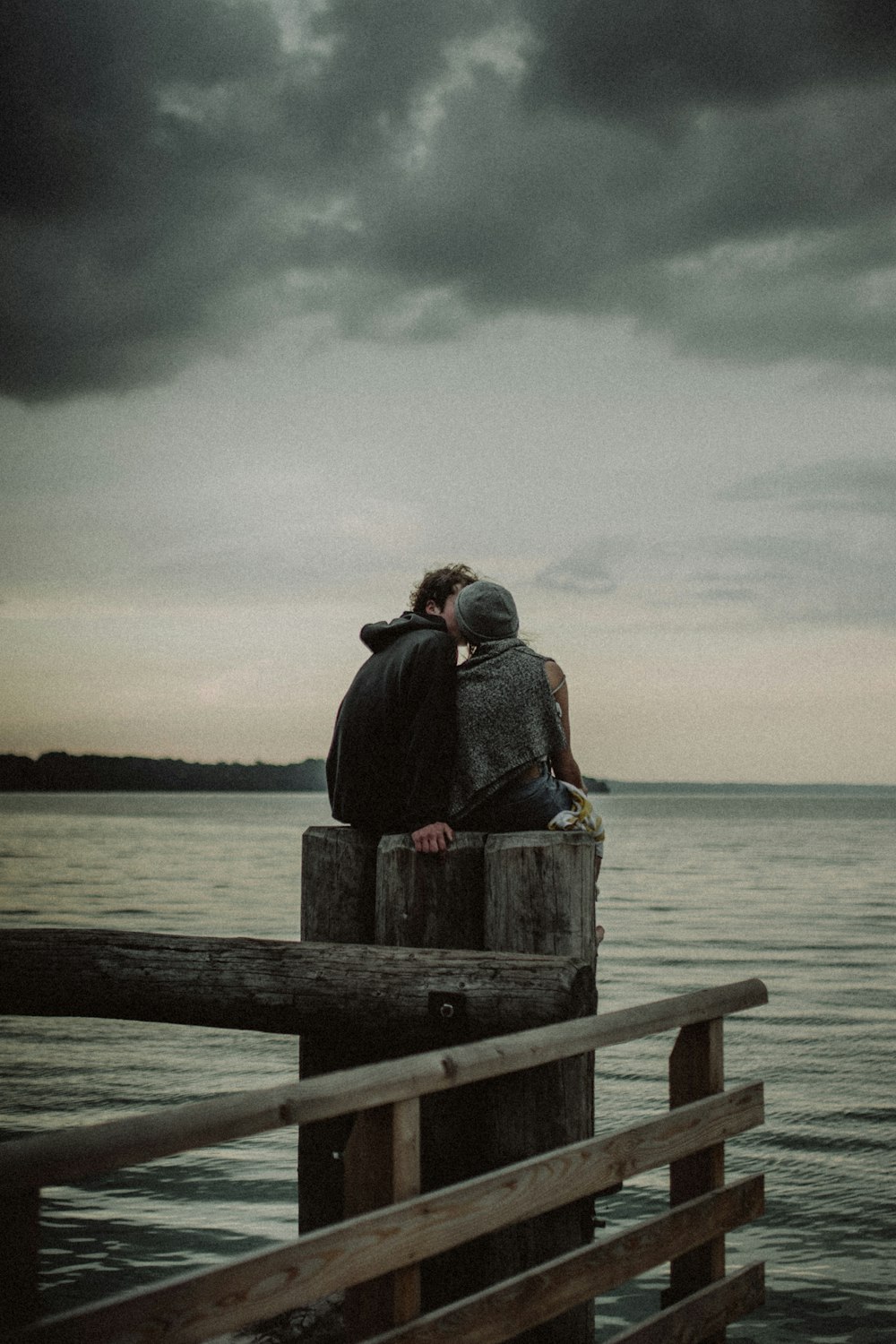 Mann und Frau sitzen und küssen sich auf einem Pfosten in der Nähe des Gewässers