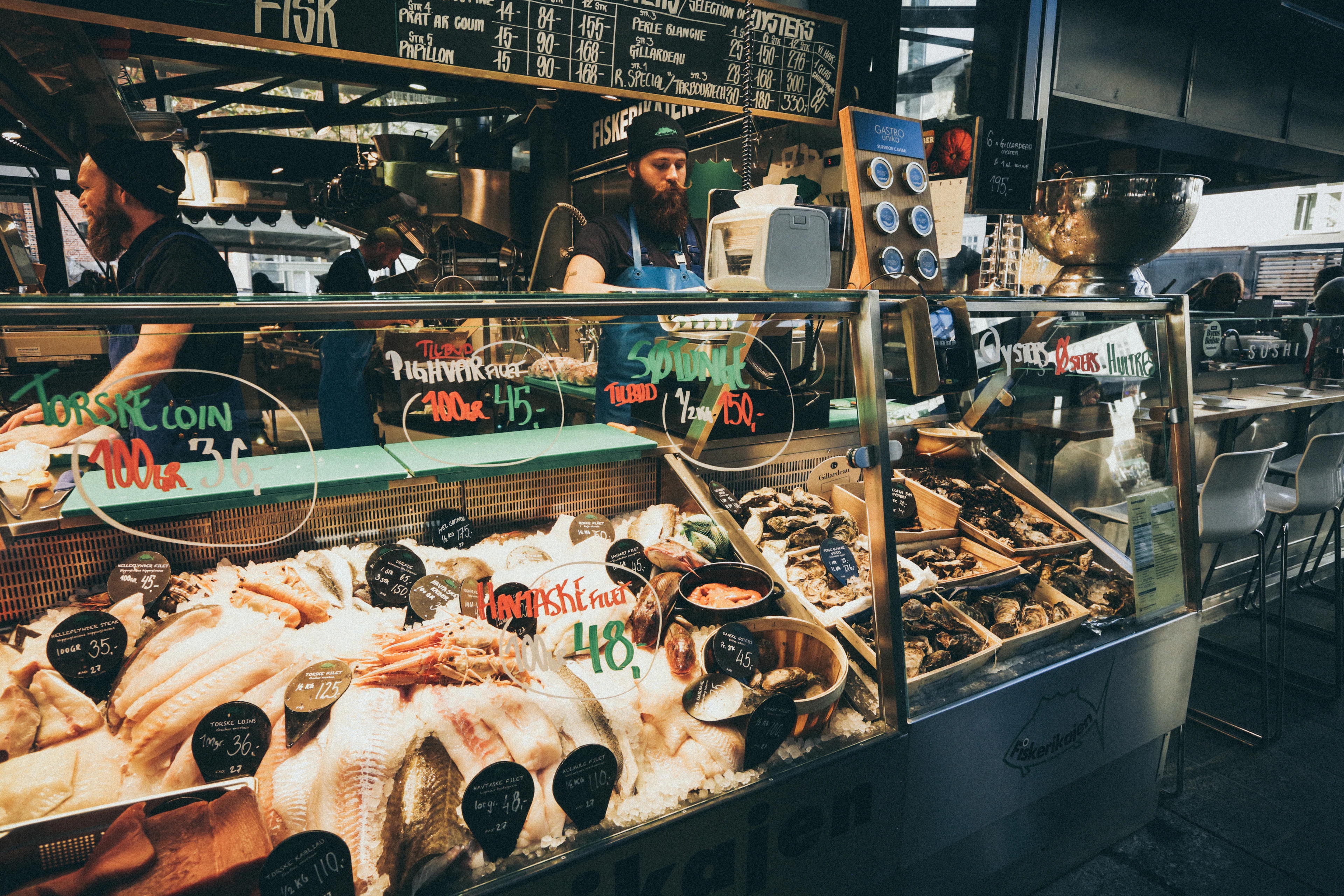 A seafood counter piled with fish and shellfish, prices chalked in Danish kroner, at a Copenhagen food market